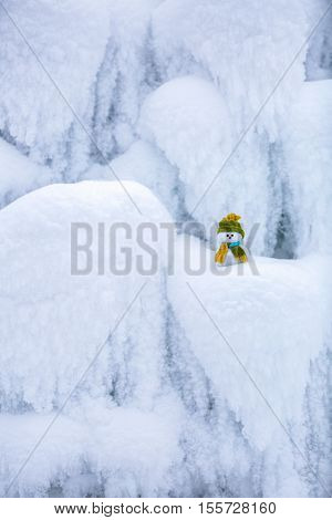 Incredible beautiful interesting white snow froze in strange textures forms and snowflakes and among all this beauty there is a little snowman in a hat and scarf.
