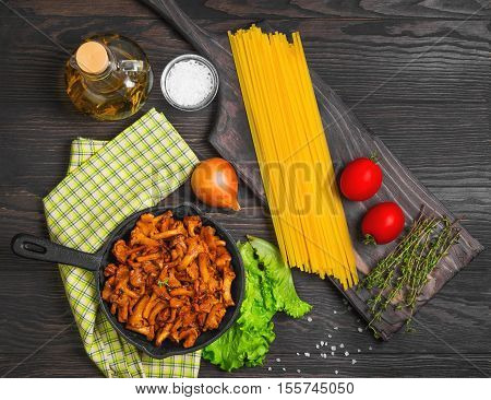 Raw not cooked Pasta spaghetti Tagliatelle with mushrooms chanterelles. Mushrooms chanterelles pasta. Ingredients for pasta spaghetti mushrooms tomatoes thyme oil. Dark wooden background. Top view