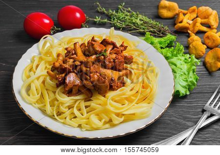 Pasta spaghetti Tagliatelle with mushrooms chanterelles. Fresh mushrooms chanterelles pasta on table. Ingredients for pasta spaghetti mushrooms tomatoes thyme lettuce. Dark brown wooden background.