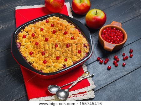 Dessert pie crumble cake apples red berries cranberries. Fresh apples berries for pie crumble cake cloth. Red Black ceramic baking pan cake crumble. Wooden dark background.