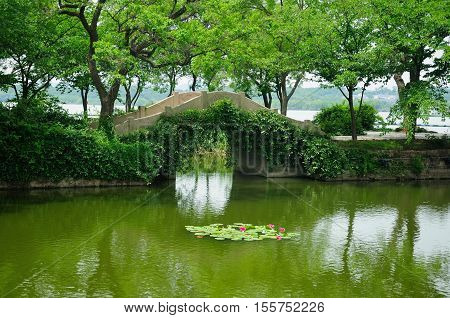 An arched stone bridge over a small pond within the Lake Tai or Taihu scenic area on Turtle island in Wuxi China on a sunny day in Jiangsu province.