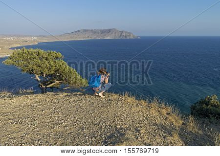Girl photographs seascape from the cliff atop Cape Alchak. Crimea September