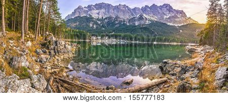 Alpine panorama with the German Alps mountains reflected in the Eibsee lake and green coniferous forest at sunset in December.