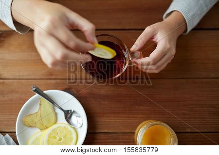 health, traditional medicine and ethnoscience concept - close up of woman adding lemon to tea cup