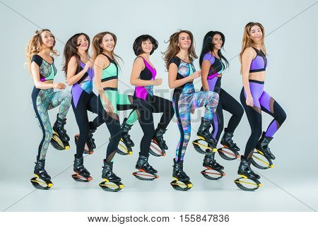 The group of young girls, jumping on kangoo training on gray