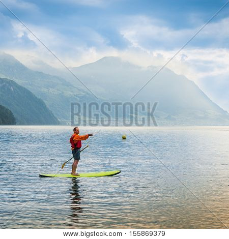Brunnen Switzerland - June 11 2013. One man stand up padling on the lake with outstretched arm points.
