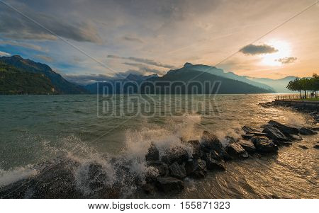Storm on the lake. Splashing waves crashing on the shore rocks. Mountains on the horizon under cloudy sky