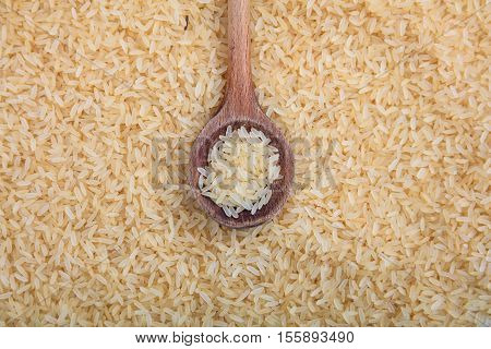A Wooden spoon on parboiled rice background