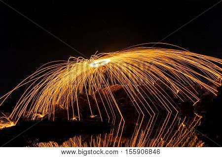 A man playing steel wool on the beach at night