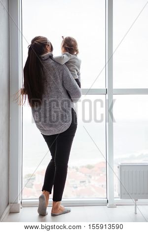?hild with casual mother near the window. from the back