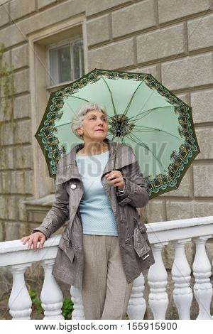 cute elderly woman senior with an umbrella on the beautiful white verandah in the park near the house