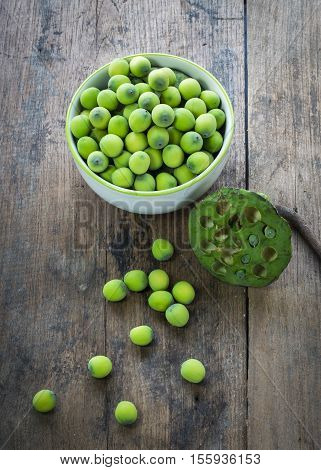 Lotus seeds in white bowl and lotuspod on wood background