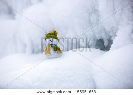 Snowman the Santa's assistant is standing in green hat wrapped with the scarf on nice textured snow on frosty winter morning.