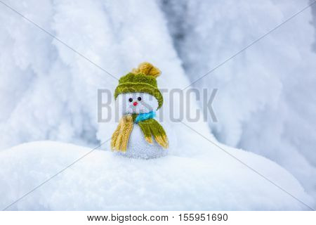 Nice dreaming snowman in green hat is standing on interesting textured snow near to the hill on cold winter day.