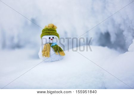 Snowman the Santa's assistant is standing in green hat wrapped with the scarf on nice textured snow on frosty winter morning.