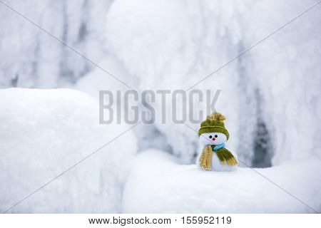 Snowman the Santa's assistant is standing in green hat wrapped with the scarf on nice textured snow on frosty winter morning.