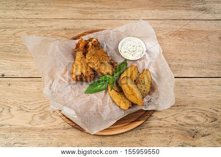 Fried fish in batter with potatoes and tartar sauce served on a wooden tray on paper