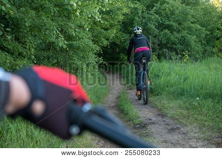 Photo From Back Of Female Bicyclist Wearing Helmet Riding Along Road In Woods During Day