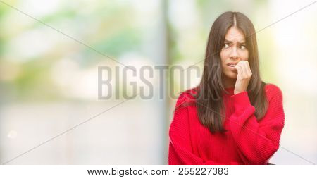 Young beautiful hispanic wearing red sweater looking stressed and nervous with hands on mouth biting nails. Anxiety problem.