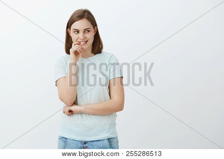 Studio Shot Of Smart And Creative Attractive Female Student With Cute Flapped Ears Biting Finger Whi