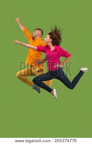 Freedom In Moving. Pretty Young Couple Jumping Against Green Background
