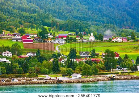 Norwegian Village Landscape With Turquoise Fjord Water, Mountains, Church And Colorful Houses. Loen,