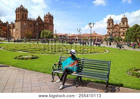 Young Female Relaxing On A Bench At Plaza De Armas With Cusco Cathedral And The Iglesia De La Compan