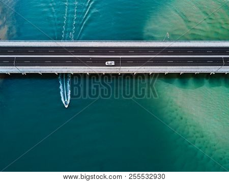 A Vehicle Drives Over The Bridge As A Speed Boat Travels Underneath Leaving A Wake Behind. Where Wil