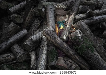 Stuffed Doll, A Scarecrow, Hidden And Abandoned Between Wood Logs, In Low Light.