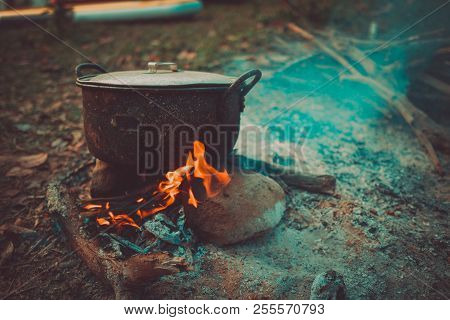 Camp And Cooking In Field Conditions, Boiling Pot At The Campfire On Picnic In Morning.  Cooking Din
