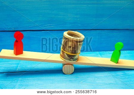 Wooden Figures Of People On Scales And Dollars Between Them. A Dispute Between Two Businessmen. Tria