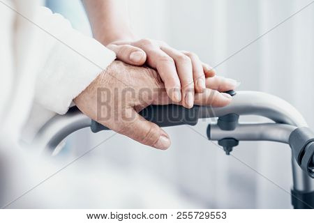 Close-up On Senior Person Hand On Walking Frame And Supporting Caregiver
