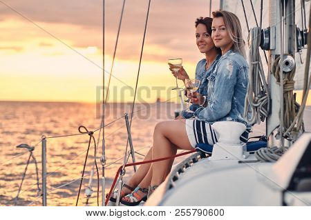 Female Friends Relaxing On The Yacht With Glasses Of Wine In The Hands, During Sunset On The High Se