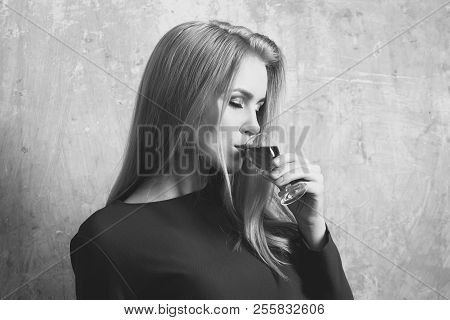 Girl Enjoying Red Liqueur In Glass. Woman With Blond Long Hair, Make Up In Blue Dress On Beige Wall.
