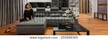 Elegant Woman Sitting On Gray Sofa In Modern Apartment With Kitchenette, Panorama