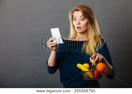 Shocked Woman Holding Shopping Basket With Fruits Looking At Bill Receipt Being Scared Of Huge Price