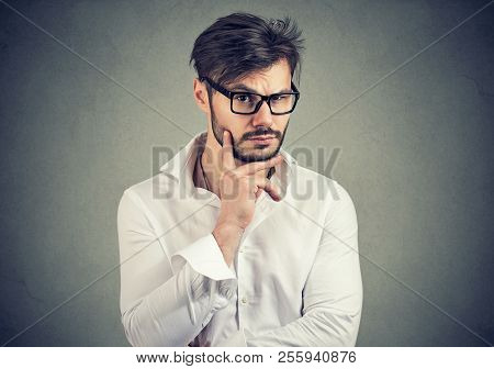 Handsome Young Man With Beard In Eyeglasses Looking Dubious And Curious On Gray Background