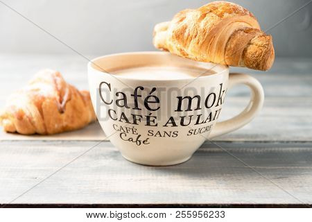 French Breakfast Is A Large Beige Cup Of Coffee With Milk And Croissants On A Wooden Table. On The C