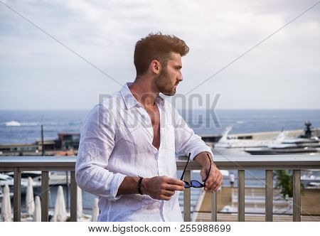 Attractive Fit Athletic Young Man Soaking In The Sun On Seaside Boardwalk Or Seafront, Wearing White