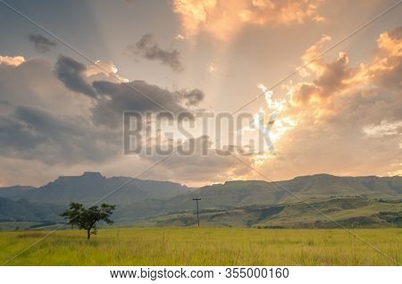 A Panoramic Of Champagne Castle Mountain And Surrounding Hills With A Grassy Foreground And Colorful