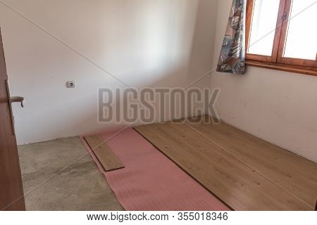 Installing Wooden Laminate Flooring With Pink Insulation Sheets In An Empty Room.