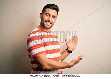 Young handsome man wearing casual striped t-shirt standing over isolated white background Inviting to enter smiling natural with open hand