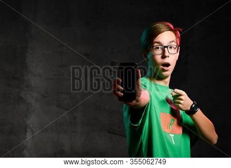 Surprised Teen Boy In Green T-shirt And Glasses Standing, Showing His Phone Screen And Feeling Disap