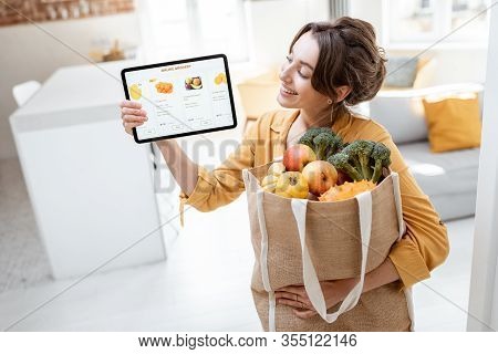 Happy Woman Holding A Digital Tablet With Launched Online Store While Standing With Shopping Bag Ful