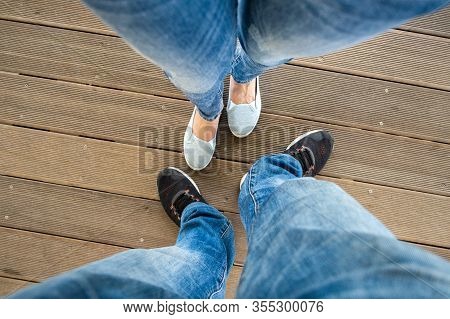 Top Down View Of Legs In Denim Jeans Pants And Light Summer Sneakers Standing On Wooden Floow.