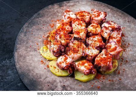 Traditional Spanish pulpo a la gallega with barbecued octopus, potato chips and chili as closeup on a modern design plate with copy space left 