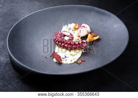 Traditional Italian polpo alla griglia su crema di patate with barbecued octopus, potato creme and vegetable chips as closeup on a modern design plate 