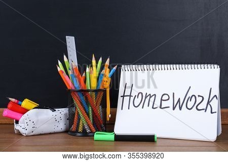 Stationery And Notebook With Inscription Homework On Wooden Table Near Blackboard