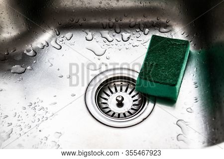 Stainless Steel Kitchen Sink And Green Sponge For Dishes. Drops Of Water On Metal