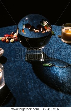 Crystal Ball, Candles And Fortune Telling Stones On Dark Blue Velour Cloth Isolated On Black